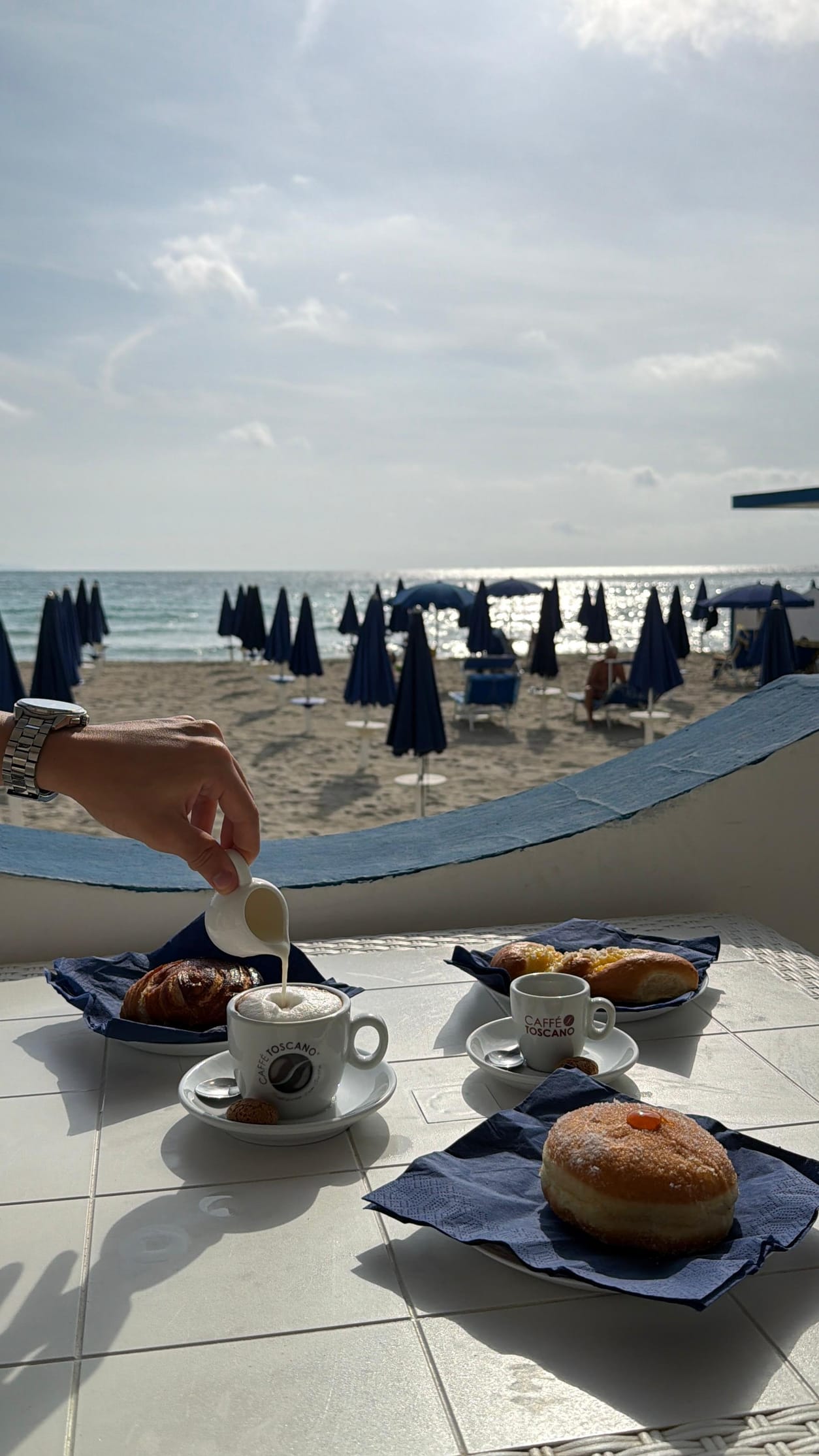 Colazione con vista sul mare del Poetto, mano che versa il latte nel cappuccino