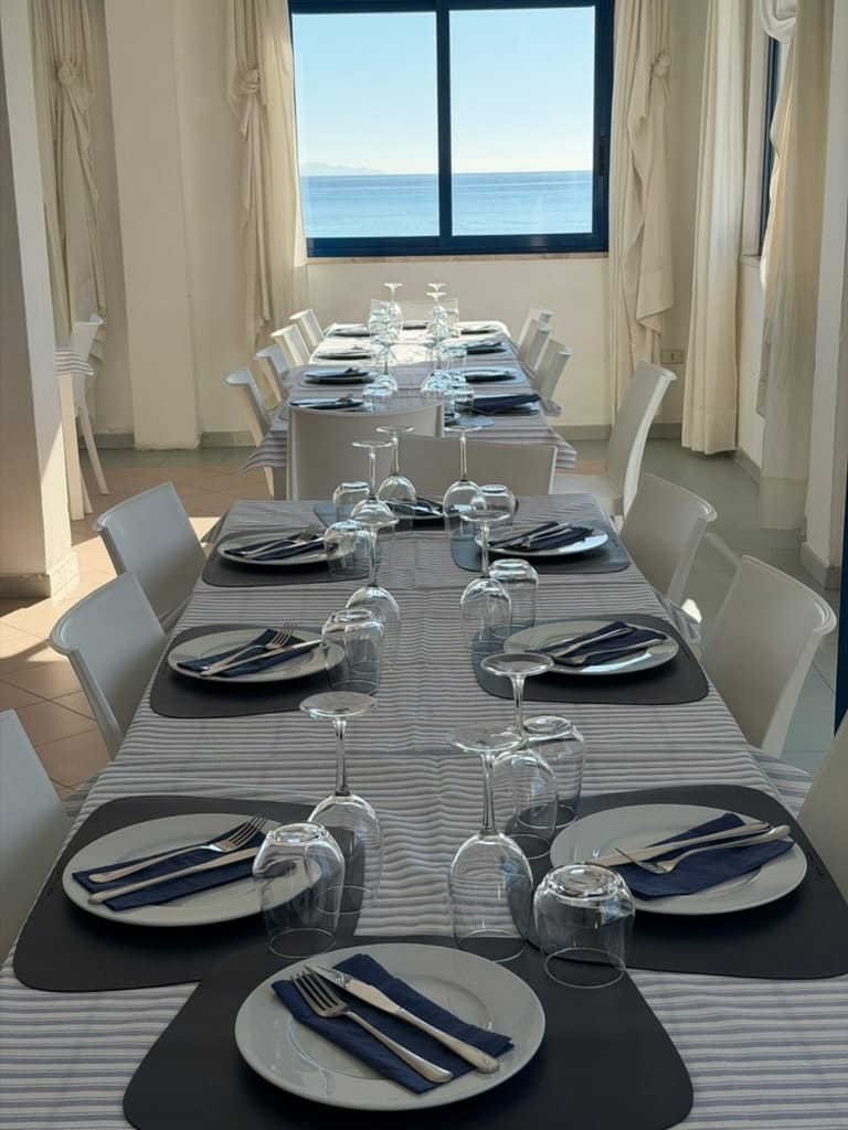 Tavolata apparecchiata per un gruppo con la finestra sul mare in fondo